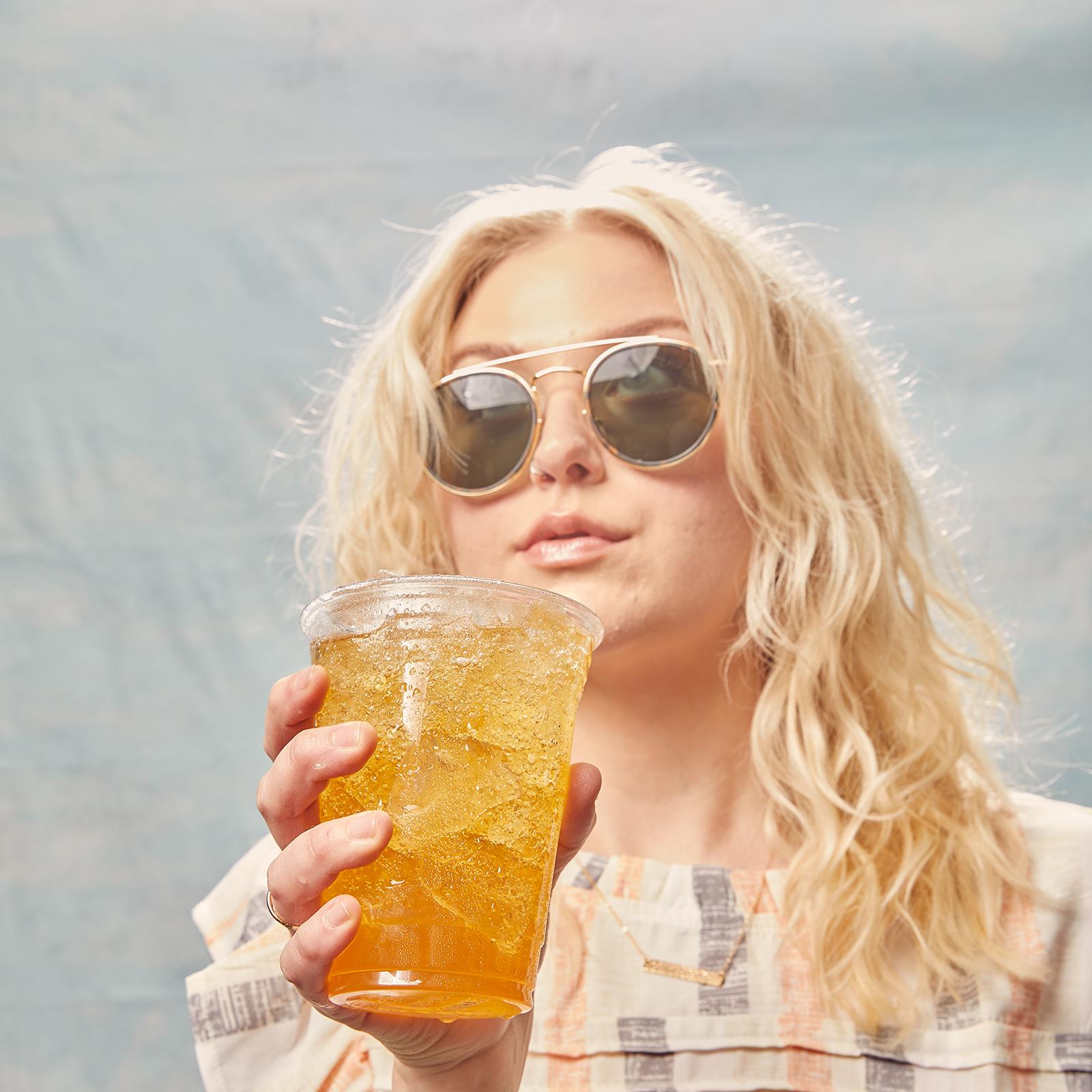 girl holding a sheetz refresher drink on a blue background