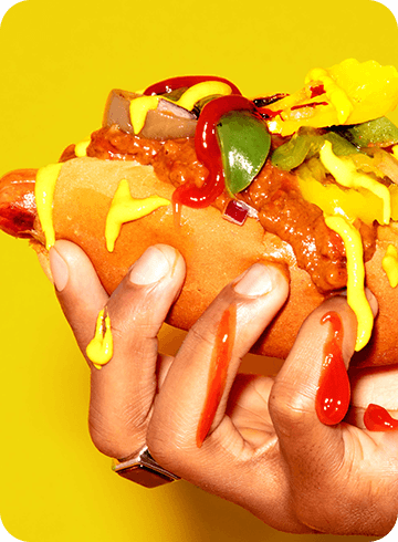 hot dog being held up in front of a yellow background