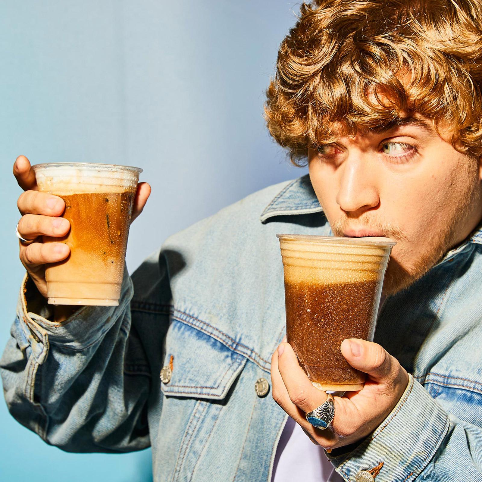 male holding two coconut nitro cold brews in front of a blue background